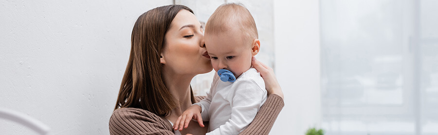 Woman kissing her small son with a pacifier at home